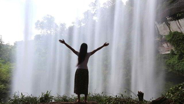 A woman with arms raised in front of a waterfall